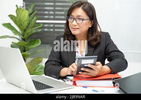 Asian accountant working and analyzing financial reports project accounting with calculator in modern office, finance and business concept. Stock Photo