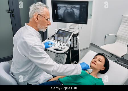 Ultrasound diagnostics of endocrine system and human thyroid. Female patient receives thyroid diagnostics with endocrinologist Stock Photo