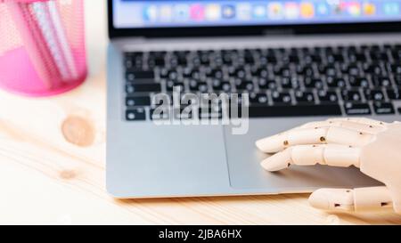 Robotic arm using laptop on a wooden table. Artificial intelligence robot working on an open laptop. Futuristic robot hand typing and working with lap Stock Photo
