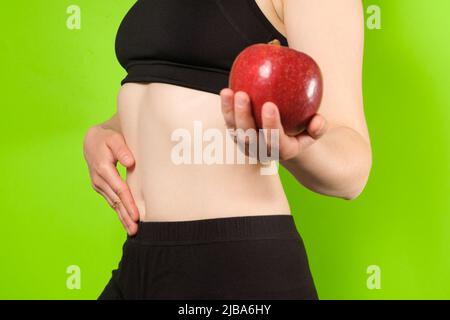 A woman on a green background holds a red apple in her hand. The concept of proper nutrition, digestion, fruit diet or raw food diet Stock Photo