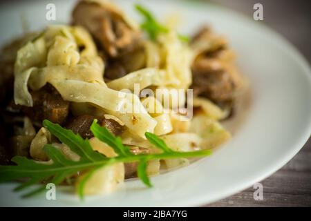 Homemade boiled noodles with meat and eggplant in a plate on a wooden table Stock Photo