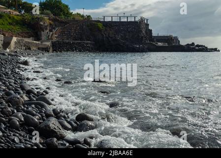 Part of the beach near funchal with the sea polished volcanic rocks in foreground and an old wall in background. Focus on foreground. Stock Photo