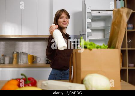 Young woman with a bottle of milk in the kitchen puts food in the refrigerator after shopping Stock Photo