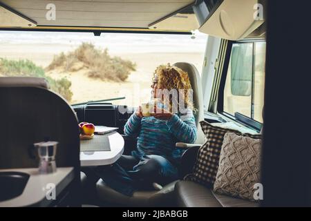 Serene adult woman admiring nature beach sitting inside a modern camper van in travel holiday vacation. Pretty young female people in van life Stock Photo