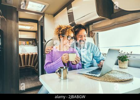 Modern couple use together laptop inside camper van. Computer leisure people surfing the web. Traveler planning next destination smiling and enjoying Stock Photo