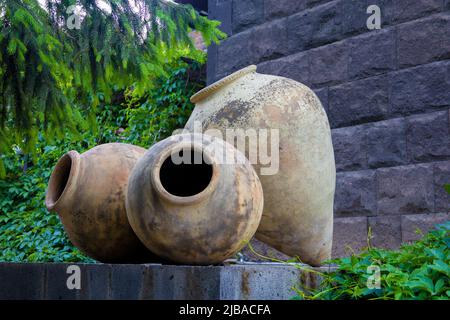 Three large pitchers on a stone base, with a stone wall and green trees in the background Stock Photo