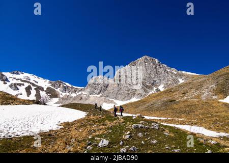 Italy Marche Sibillini National Park - Hikers on the path that leads to the Laghetto di Palazzo Borghese. In the background the massif of Palazzo Borghese Stock Photo