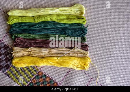 Set of multi-colored cotton threads and fragment of colorful cross-stitch embroidere. Top view. Colorful mouline threads. Close-up. Selective focus. Stock Photo