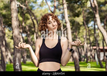 Cute caucasian woman wearing sports bra standing on city park, outdoor clueless and confused with open arms, shrugging shoulders, no idea and doubtful Stock Photo