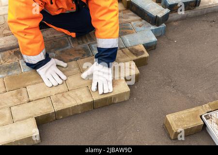 a worker in a protective work suit lays paving slabs. A professional Stock Photo