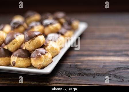 Profiteroles with cream and chocolate. Eclairs with black chocolate on wooden background. Traditional French dessert. Selective focus. Stock Photo