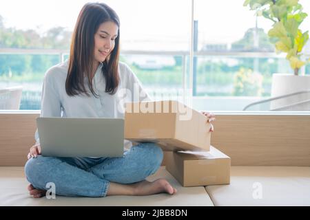 Happy young Asian woman entrepreneur, Smile for sales success after checking order from online shopping store in a laptop at home office, Concept of m Stock Photo