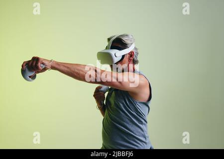 Athletic senior man playing a virtual reality fitness game. Mature man doing workout exercises using a pair of gaming controllers. Sporty senior man w Stock Photo