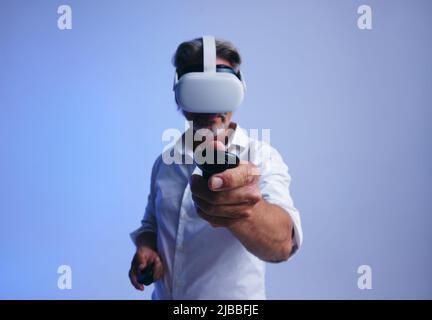 Getting business done in the metaverse. Senior businessman using a remote control to press a button in virtual space. Mature businessman wearing a vir Stock Photo