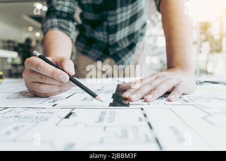 Interior designer or architect reviewing blueprints and holding pencil drawing on desk at home office. Stock Photo