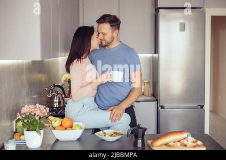 Caucasian young happy couple hugging and having coffee in morning on weekend. Love concept. Stock Photo