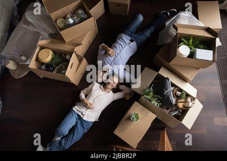 Overhead view homeowners couple lying on floor near cardboard boxes Stock Photo