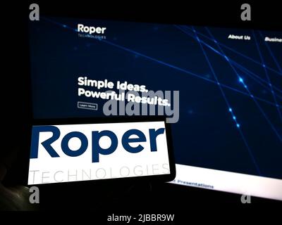 Person holding smartphone with logo of US engineering company Roper Technologies Inc. on screen in front of website. Focus on phone display. Stock Photo