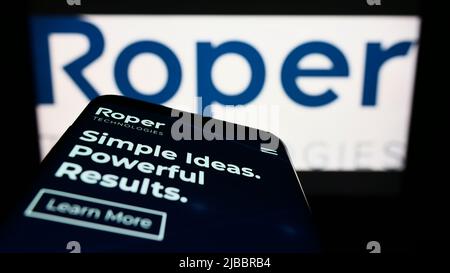 Mobile phone with website of American engineering company Roper Technologies Inc. on screen in front of logo. Focus on top-left of phone display. Stock Photo