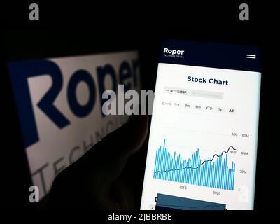 Person holding cellphone with webpage of US engineering company Roper Technologies Inc. on screen with logo. Focus on center of phone display. Stock Photo