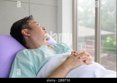 Asian patient man lying in hospital bed and looking at distance Stock Photo