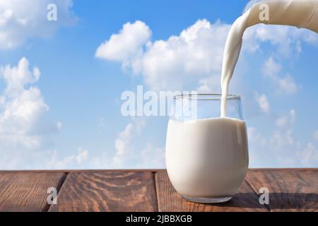 milk pouring from jug into glass on table Stock Photo