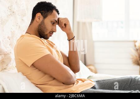 Side View Of Unhappy Depressed Arabic Man Sitting In Bedroom Stock Photo