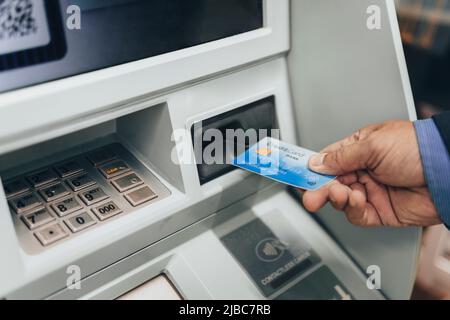 Closeup of man's hand inserting e-card into ATM slot Stock Photo