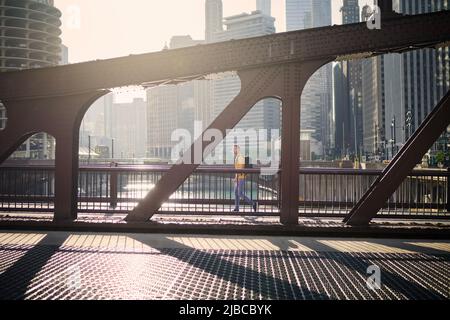 Side view of man on the move while walking on bridge and looking around. City in morning light. Stock Photo
