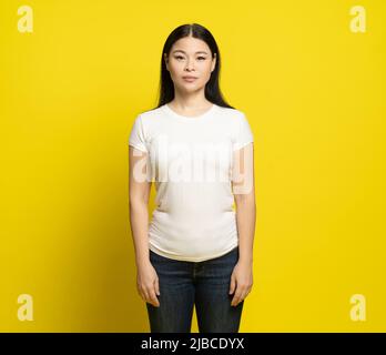 Sad asian woman with long hair wearing white t-shirt and jeans standing happy laughing isolated on yellow background. Fashion concept.  Stock Photo