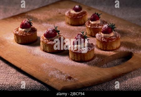 Muffins on a wooden board decorated with cream and strawberries and with powdered sugar Stock Photo