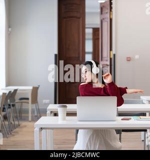 Asian female student doing gymnastics exercises, resting from computer screen during online classes Stock Photo