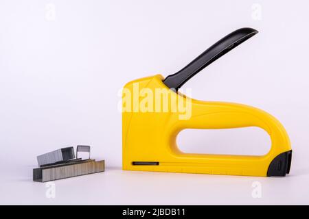 Yellow staple gun and metal staples on a white background. Stock Photo