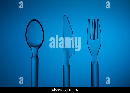 Set of plastic transparent spoon, knife and fork on a blue background. Studio shot. Stock Photo