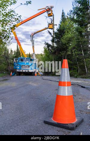 Selective focus view of a traffic cone as blurry contractors are seen at work in background, repair power line in aftermath of stormy weather. Stock Photo