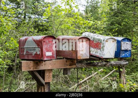 Closeup selective focus view of four old rusty mailboxes on a totting wooden post with blurry trees in background in rural village. Copy space above. Stock Photo