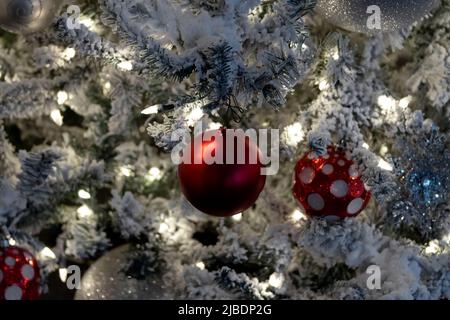 close up christmas decoration scene, white lights on snow covered tree with red and white christmas balls, festive holiday scene Stock Photo