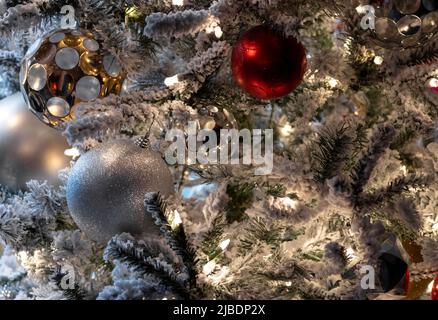 close up christmas decoration scene, white lights on snow covered tree with red and white, silver and gold christmas balls, festive holiday scene Stock Photo