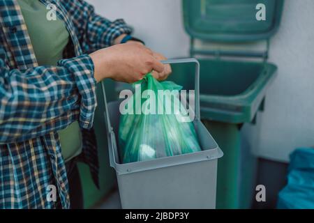 European 30s woman throwing garbage into the recycling bin in the backyard near the house. Separating recyclable garbage plastic  Stock Photo