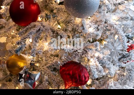 warm lighting, close up christmas decoration scene, white lights on snow covered tree with red, white, silver and gold christmas balls, festive holida Stock Photo