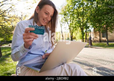 Cheerful woman doing online payments in park Stock Photo