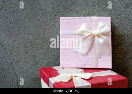 Front view of two beautiful gift boxes with satin ribbon on a background of natural concrete wall. Pink and red gift for Father's Day or Christmas. Copy space for text Stock Photo