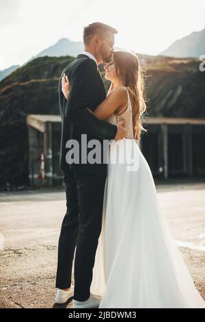 The bride and groom with stand hugging on mountains background, the groom kisses the bride on the forehead. Holiday wedding. Portrait of the bride Stock Photo