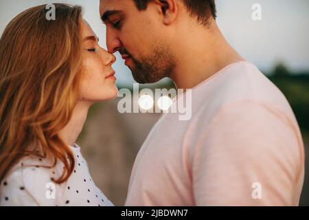 Close up portrait of a caucasian couple trying to kiss outside while dating. Lovers holiday. Love, dating. Family day. Attractive beautiful girl. Stock Photo