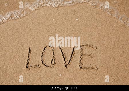 Love - handwritten on the soft beach sand. Stock Photo