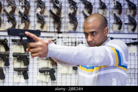 Focused latin american man aiming with pistol in gun shop Stock Photo