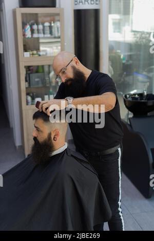 Barber doing haircut to a bearded man inside barber shop in the morning Stock Photo