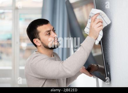 Young man wiping dust on screen of TV in living room Stock Photo