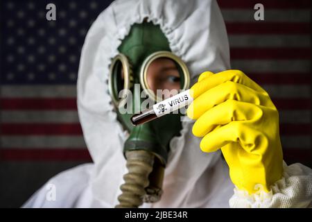 Secret lab, scientist in protective suit and gas mask holds test tube with dangerous virus on USA flag background. Concept of toxic chemical and biolo Stock Photo