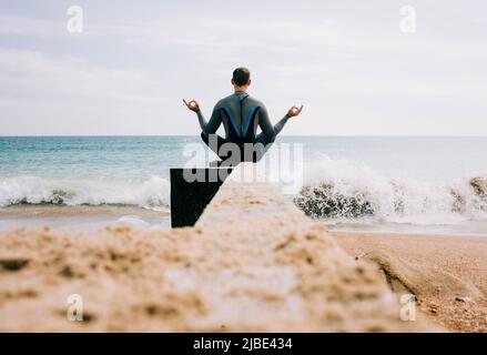 man sat meditating on a beach groyne before going swimming in the sea Stock Photo